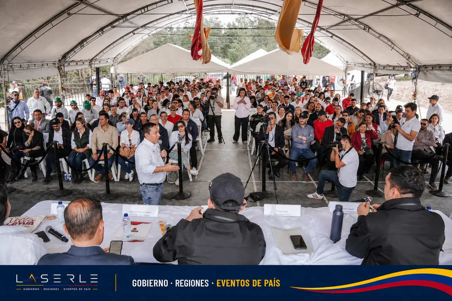 Evento público bajo carpa con panel y prensa